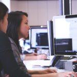 two women sitting in front of computer monitor